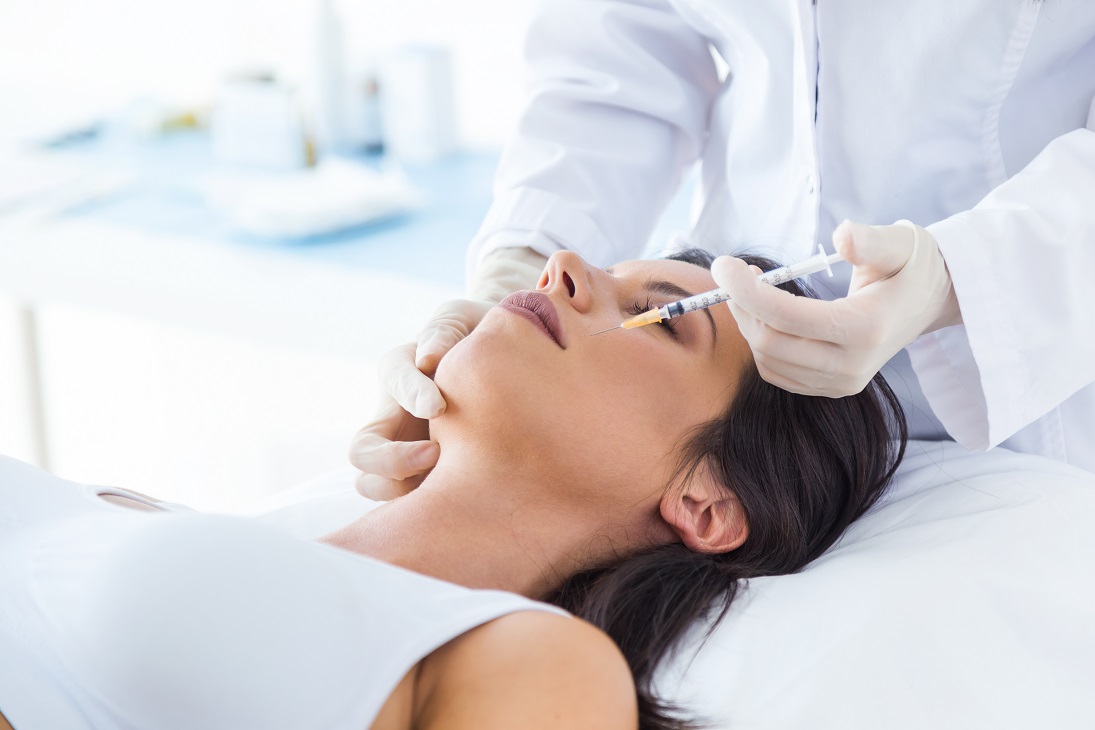 Beautiful young woman getting botox cosmetic injection in her fa