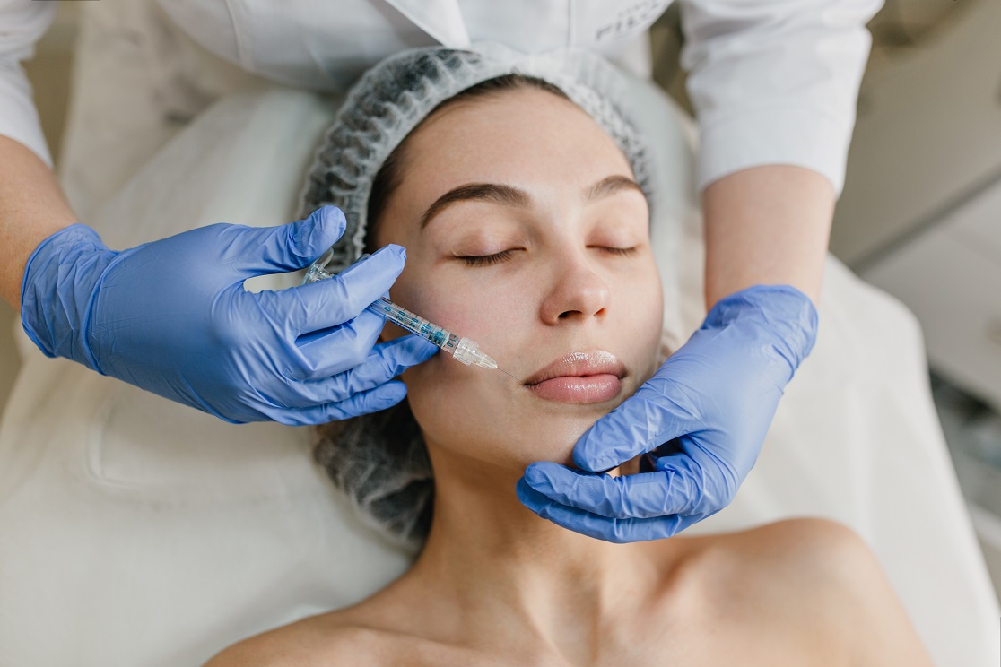 Portrait young woman during cosmetology procedures in beauty salon. Injecting, botox, hands in blue glows, healthcare, therapy, lips, beauty.