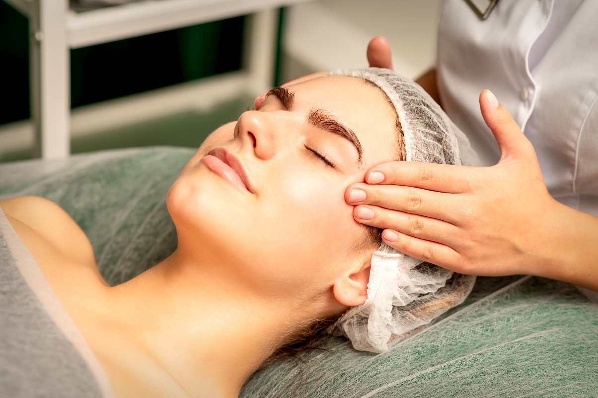 Head massage. Beautiful caucasian young white woman receiving a head and forehead massage with closed eyes in a spa salon.